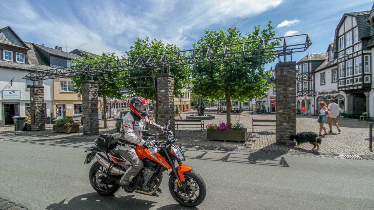 Motorrad auf einem Marktplatz mit Fachwerkhäusern und einer Pergola